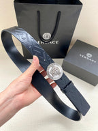 Dark leather belt with embossed pattern and round Medusa logo buckle, held up.