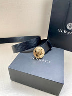 Dark leather belt with embossed texture and round Medusa logo buckle on box.