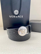 Dark leather belt with embossed pattern and round Medusa logo buckle, relaxed loop.
