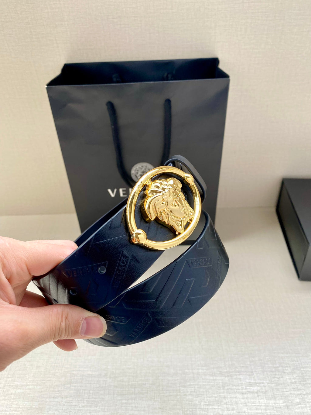 Versace belt held in hand, dark blue embossed leather with gold-tone oval buckle