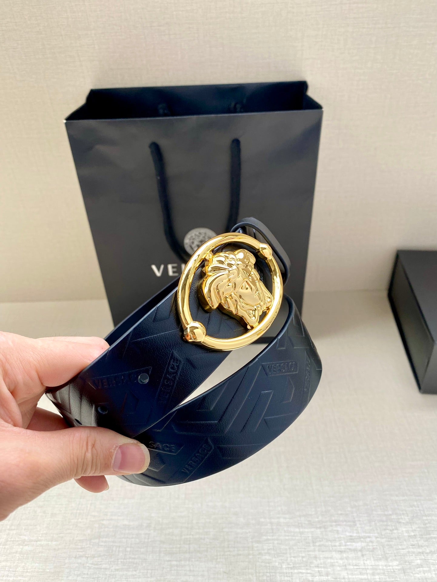 Versace belt held in hand, dark blue embossed leather with gold-tone oval buckle