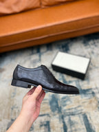 Black leather lace-up shoe held in hand, low-profile sole