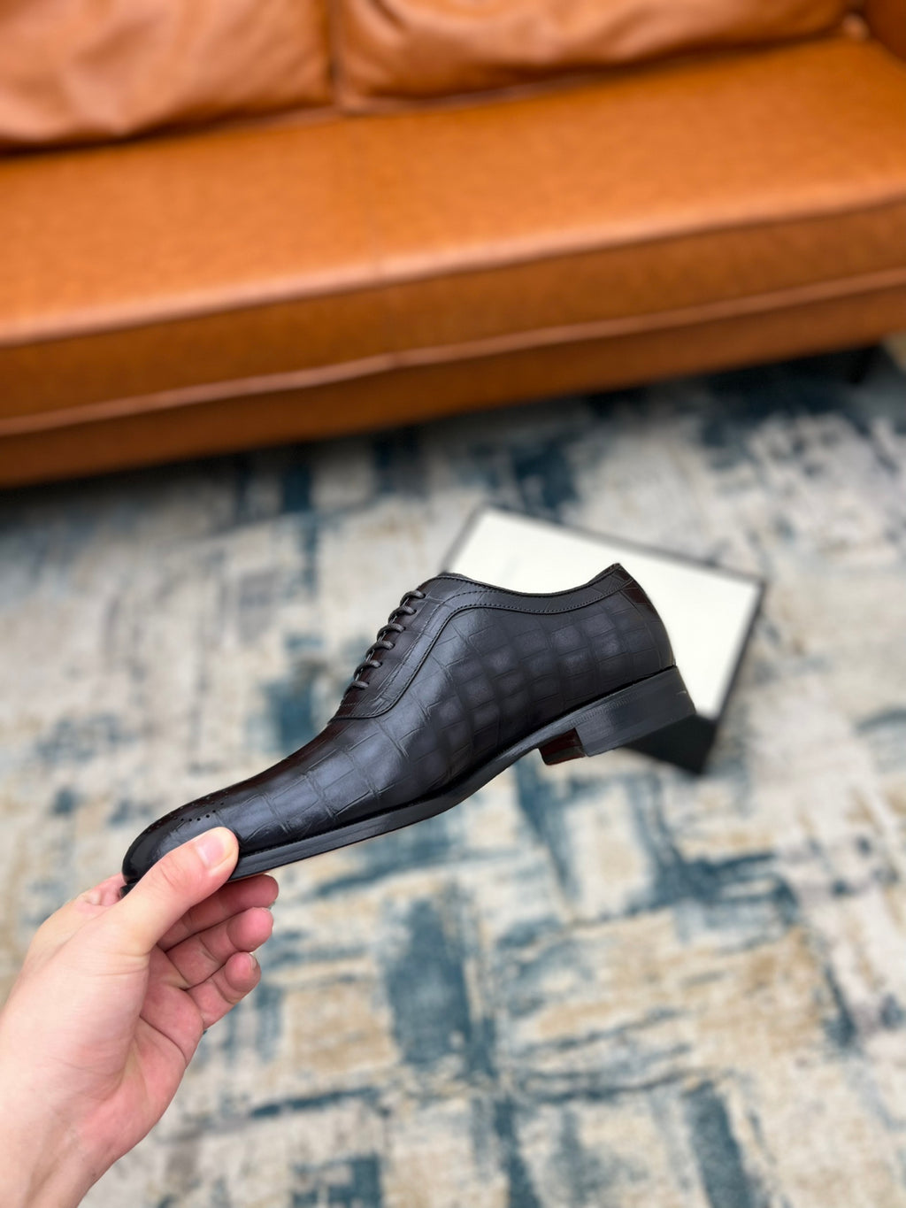 Black leather lace-up shoe held in hand, side profile