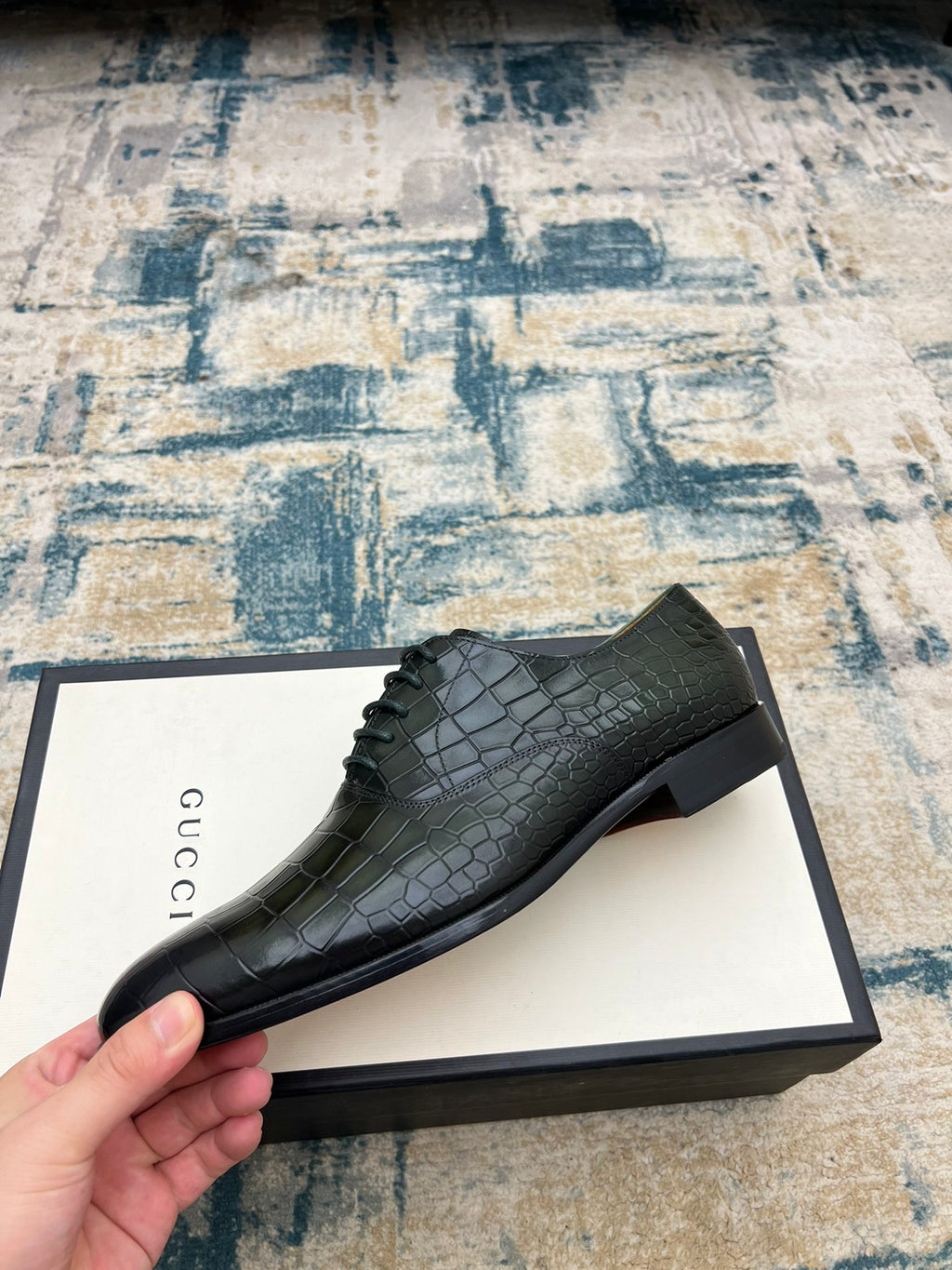Black crocodile-embossed lace-up dress shoe on branded box, side angle