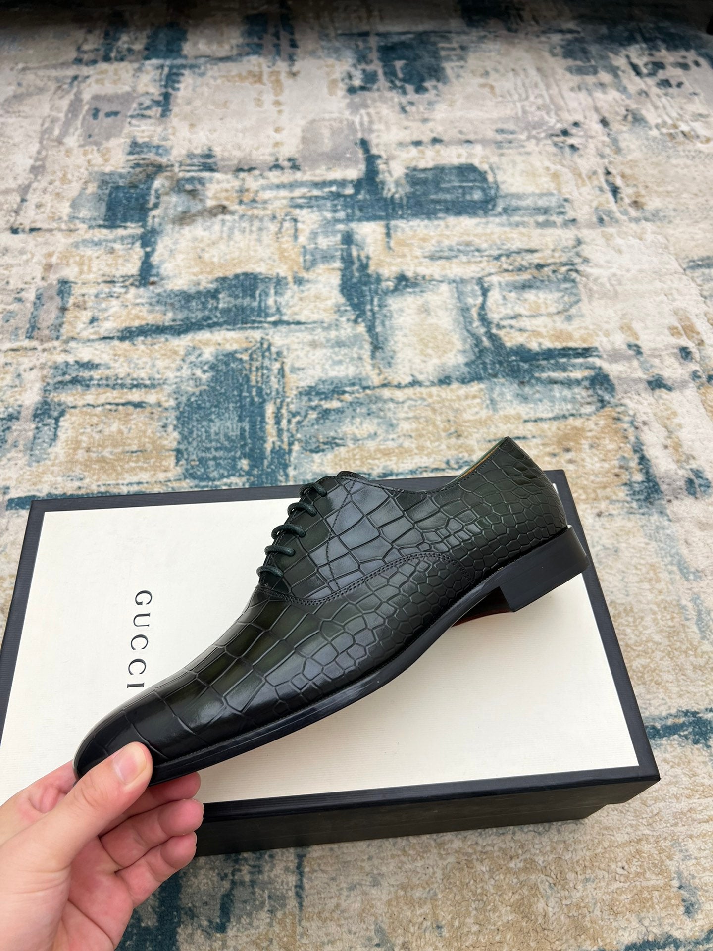Black crocodile-embossed lace-up dress shoe on branded box, side angle