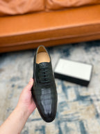 Black crocodile-embossed lace-up dress shoe held up, front close view