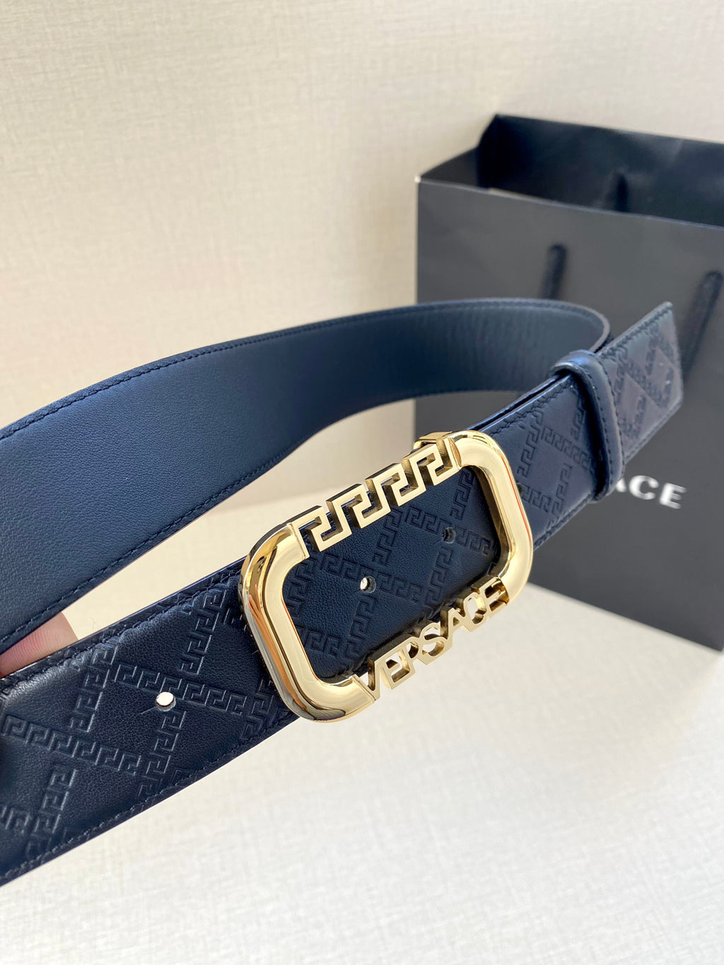 Versace belt close-up: dark blue monogram strap with gold-toned buckle detail