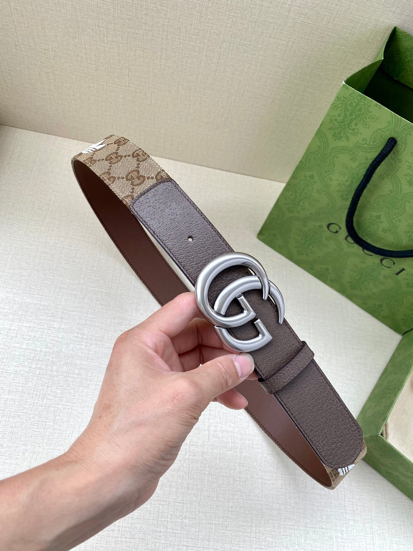 Gucci belt with brown leather strap and silver double-G buckle, held in hand