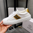 White leather low-top sneaker held in hand, gold logo panel on side