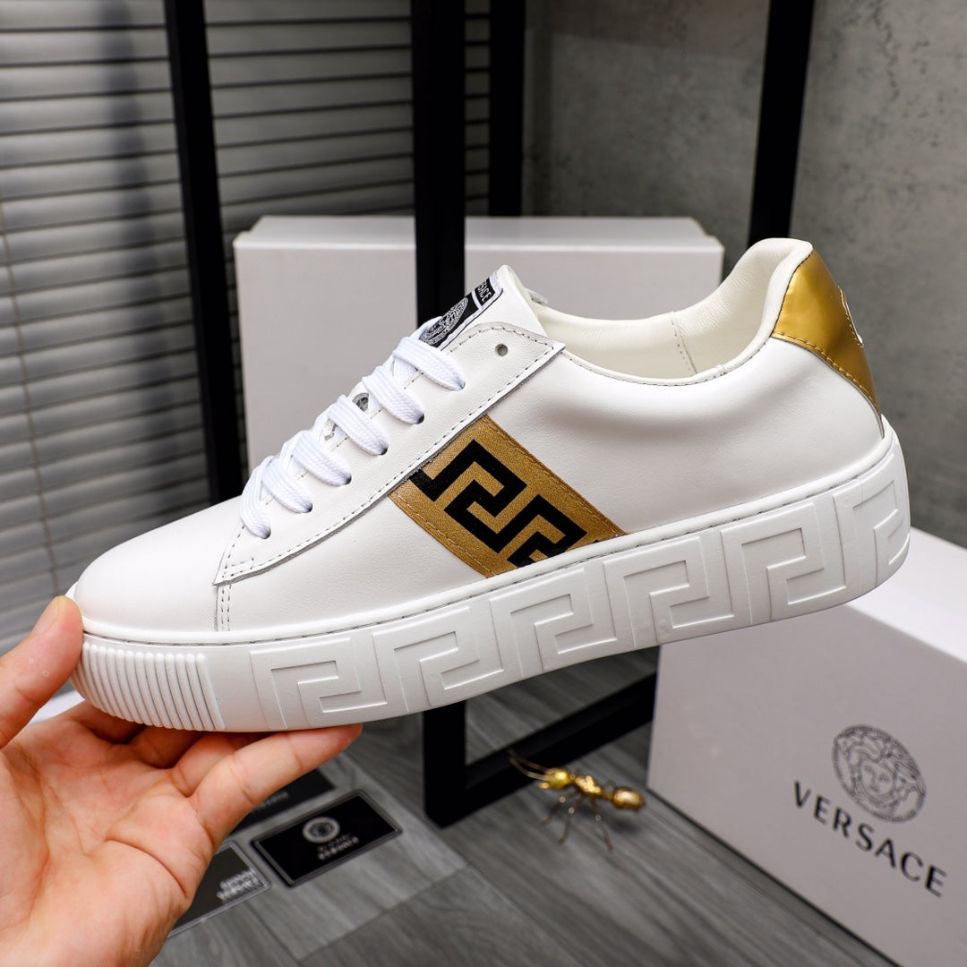 White leather low-top sneaker held in hand, gold logo panel on side