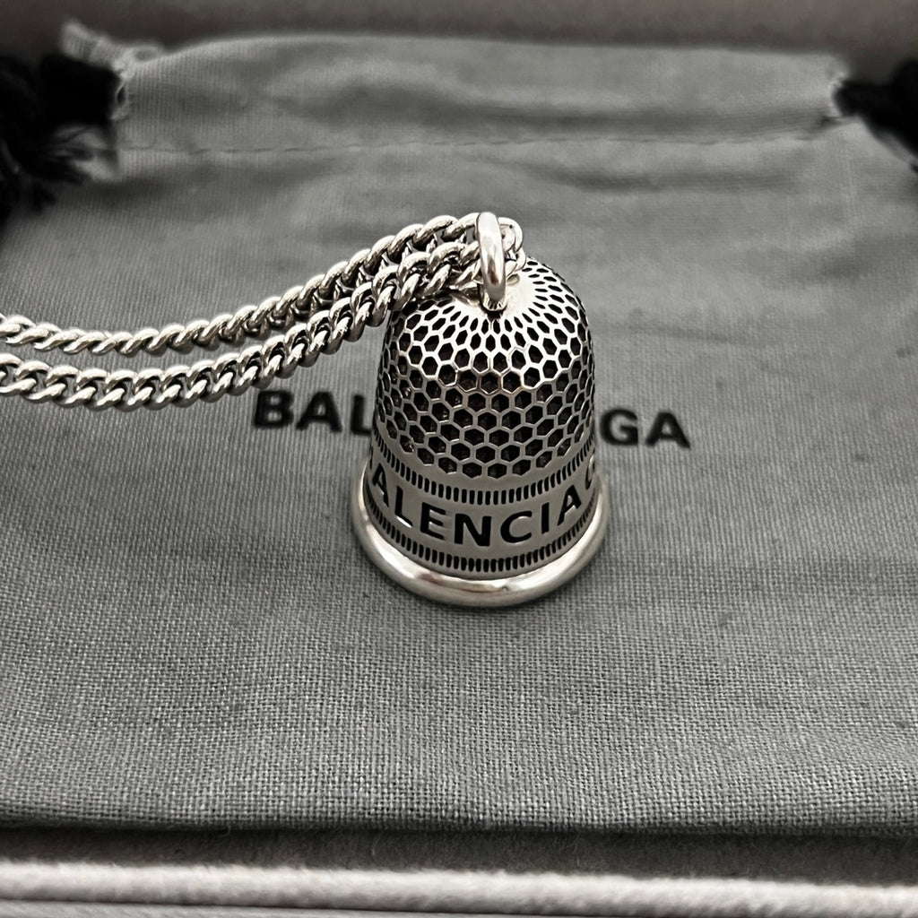 Close-up: silver mesh bell pendant on chain with logo band and 8B label