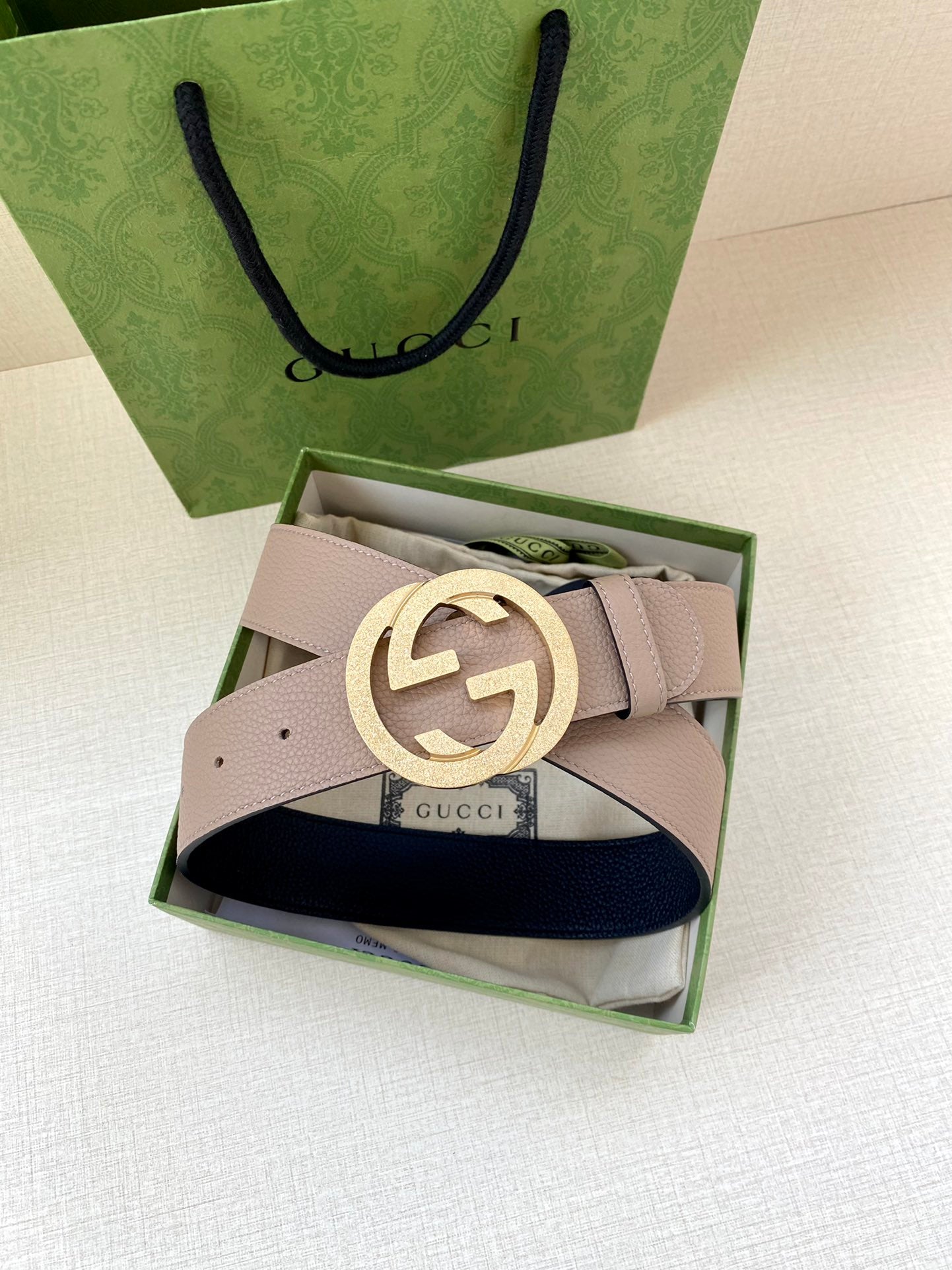 Gucci belt with taupe strap and gold-toned round G buckle over dark blue underside