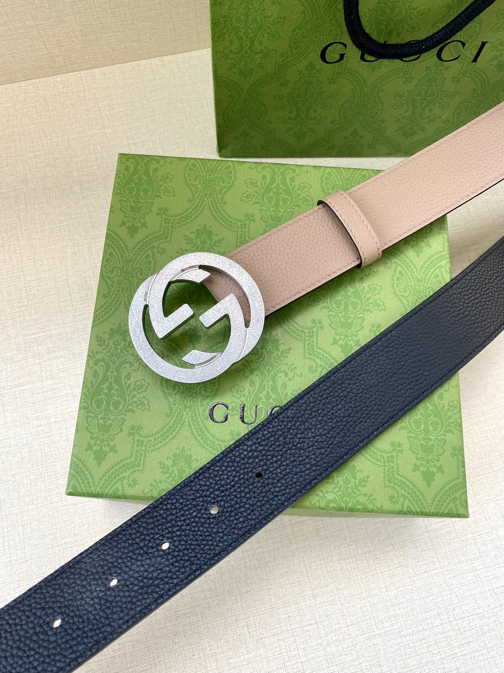 Gucci belt with light taupe strap and silver G logo buckle over dark blue strap