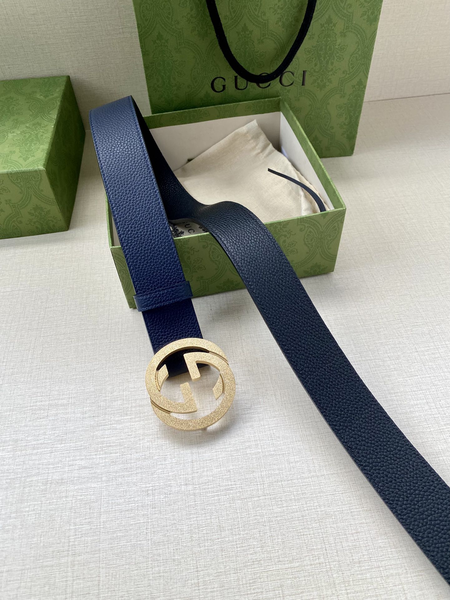 Navy leather belt with round gold logo buckle, laid flat