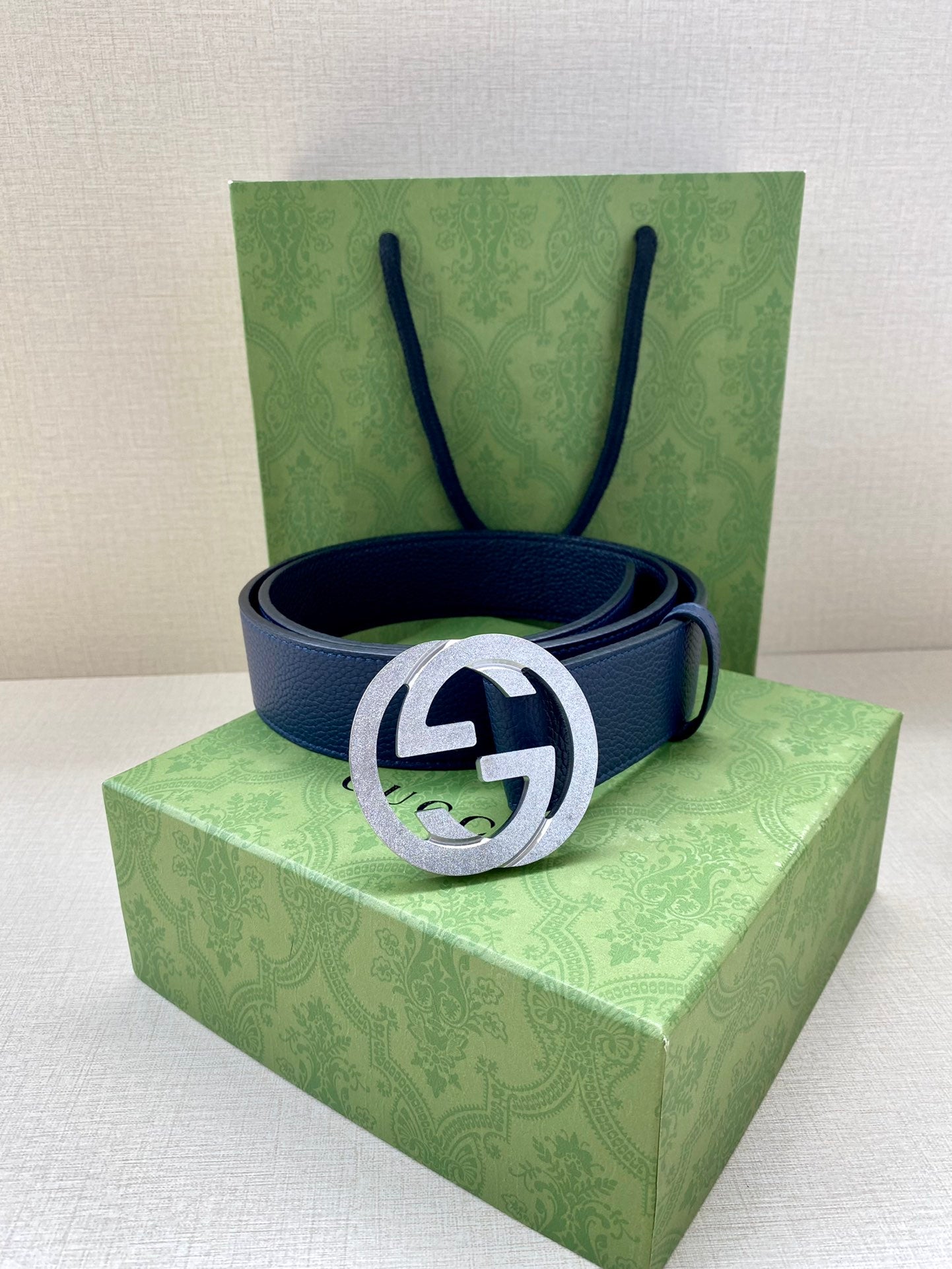Navy leather belt with round silver logo buckle resting on box