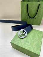 Navy leather belt with round silver logo buckle on green box lid
