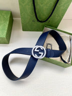 Navy leather belt with round gold logo buckle on open packaging