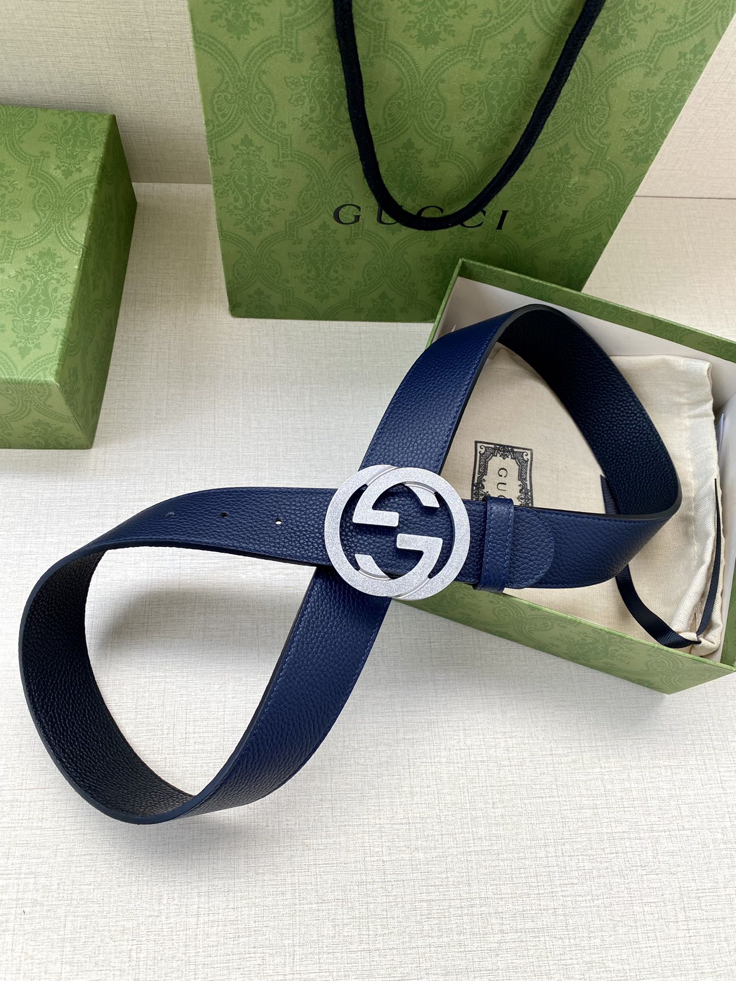 Navy leather belt with round gold logo buckle on open packaging