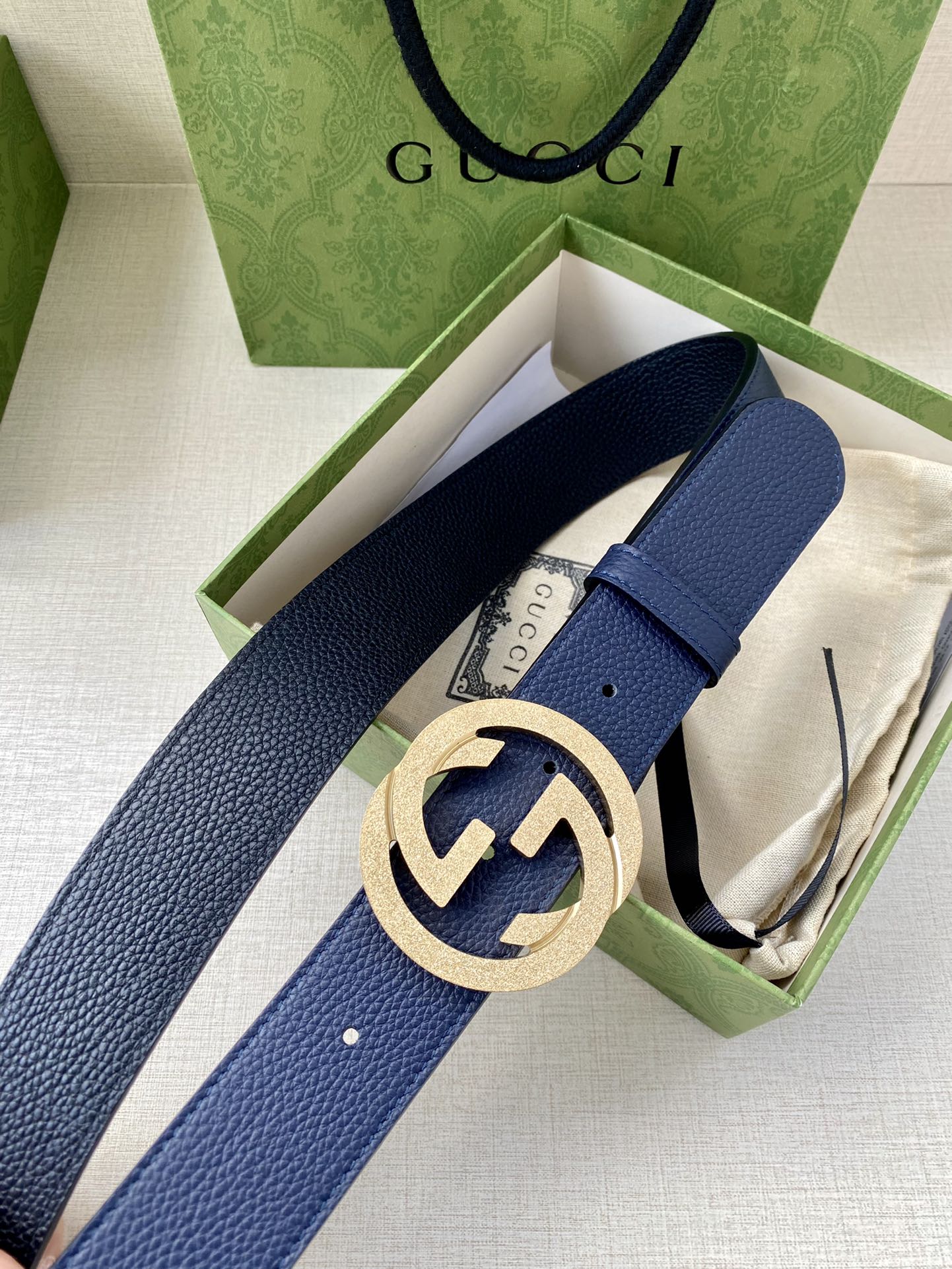 Navy leather belt with round gold logo buckle in open gift box