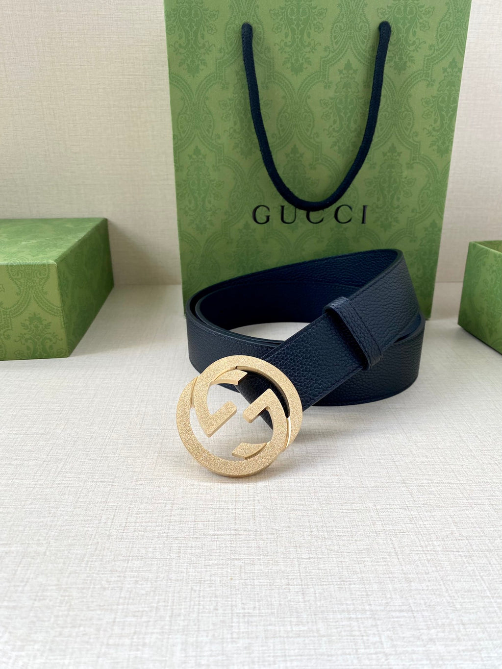 Navy leather belt with round gold GG buckle resting on surface