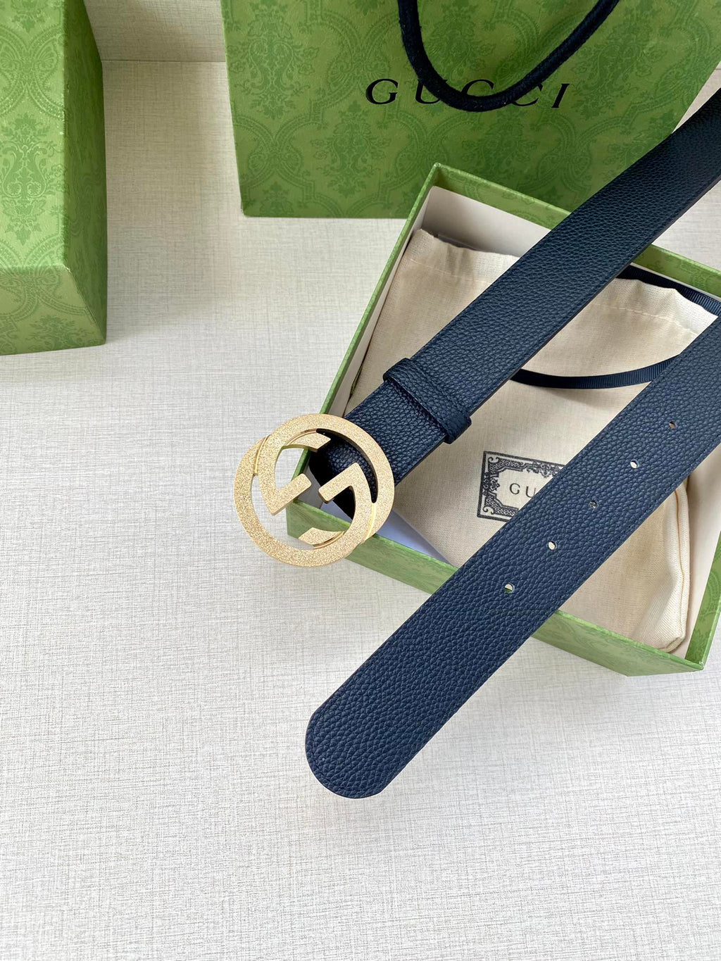 Navy leather belt with round gold GG buckle across gift box