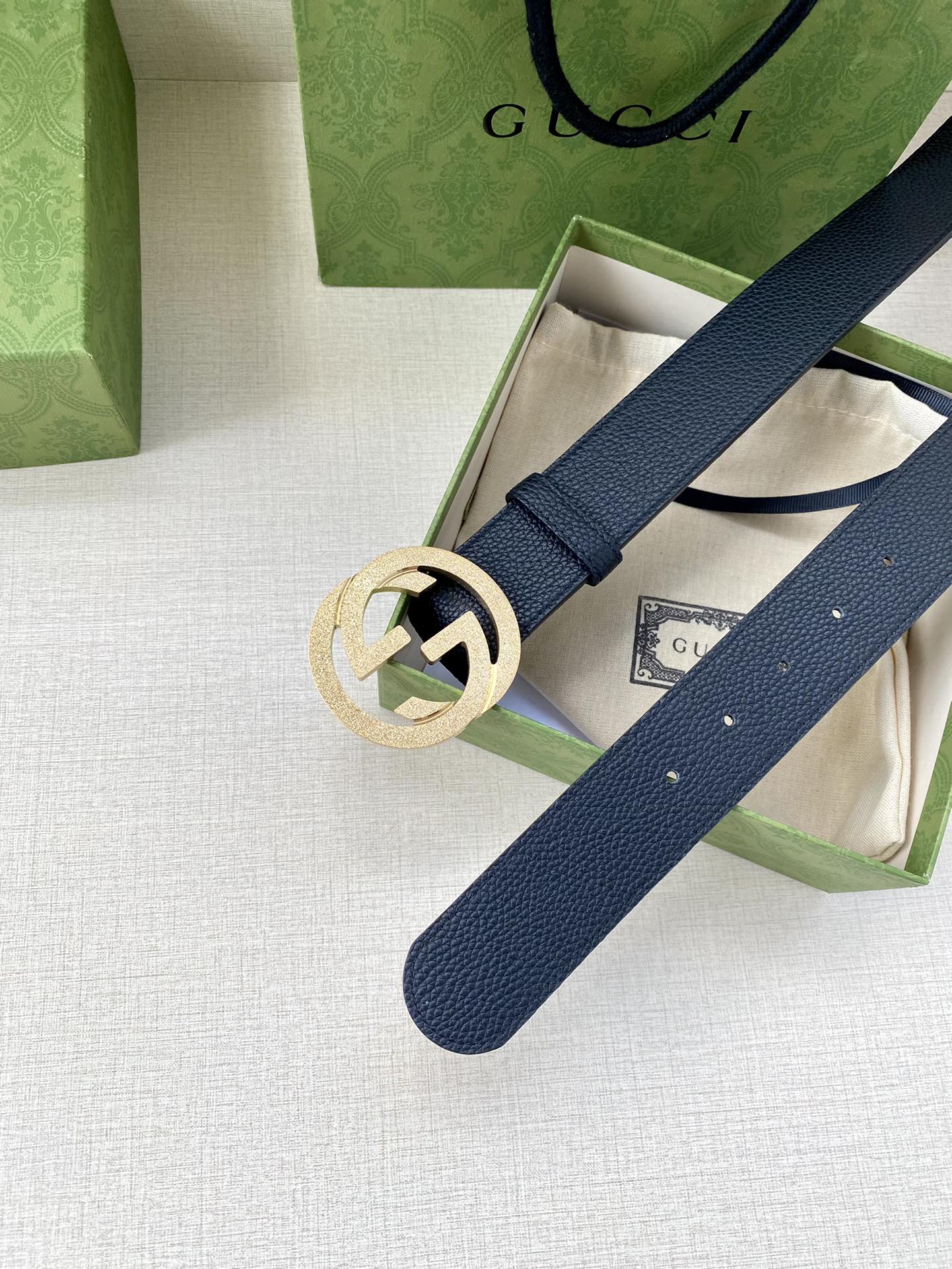 Navy leather belt with round gold GG buckle across gift box