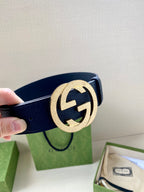 Navy leather belt with round gold GG buckle close-up, hand holding strap