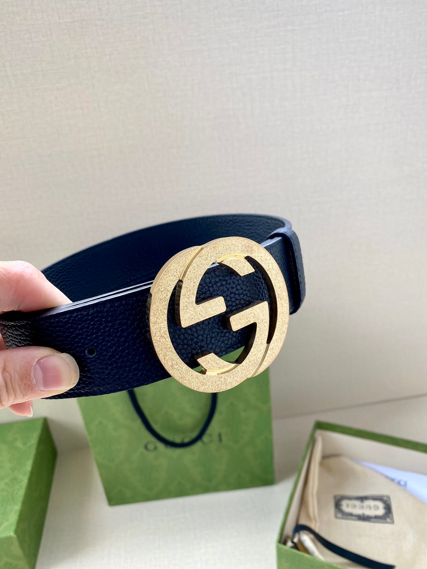 Navy leather belt with round gold GG buckle close-up, hand holding strap