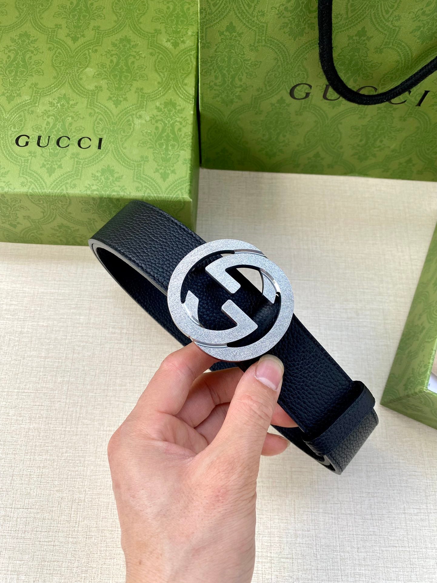 Navy leather belt with round silver GG buckle, held in hand