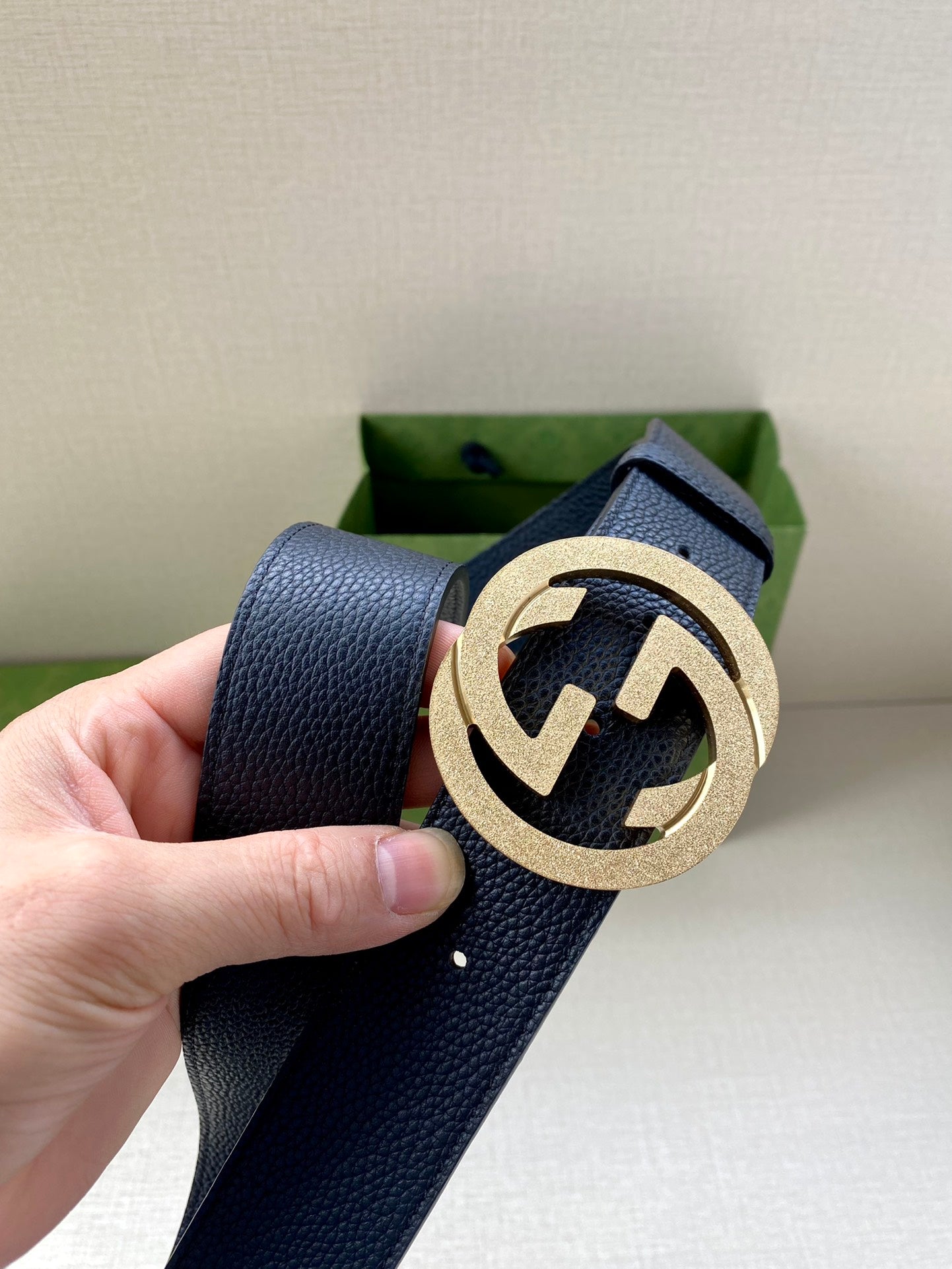 Navy leather belt close-up with round gold GG buckle held by hand