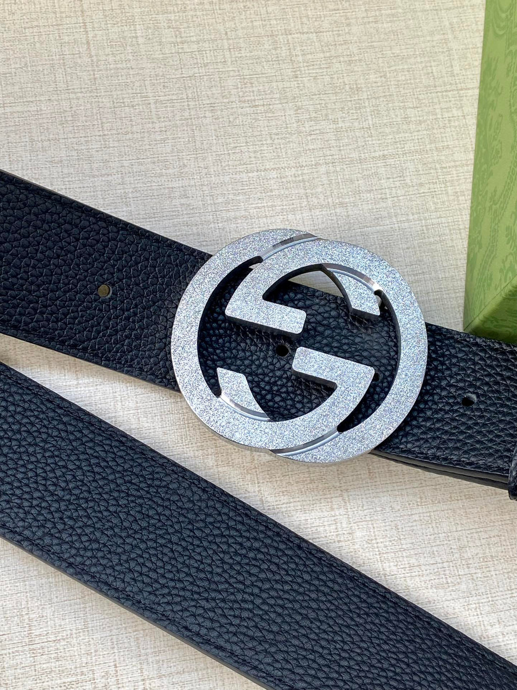 Navy leather belt close-up with round silver GG buckle and pebble texture