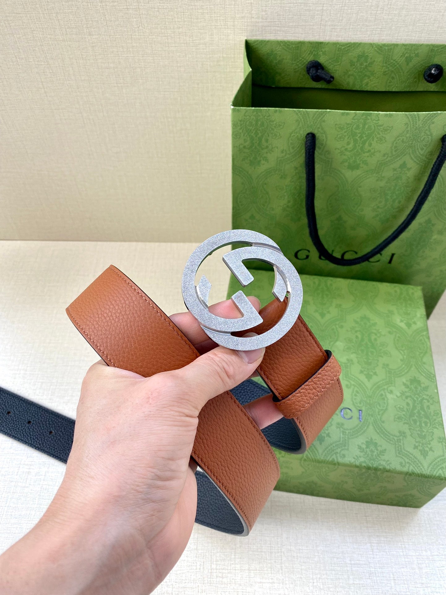 Gucci belt with tan leather strap and silver GG buckle, hand holding
