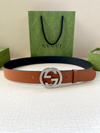 Gucci belt with tan leather strap and silver GG buckle, laid on table