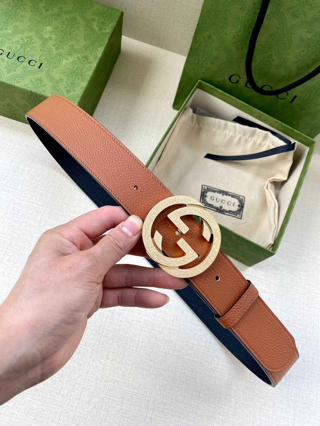 Gucci belt with tan leather strap and silver GG buckle, shown in hand