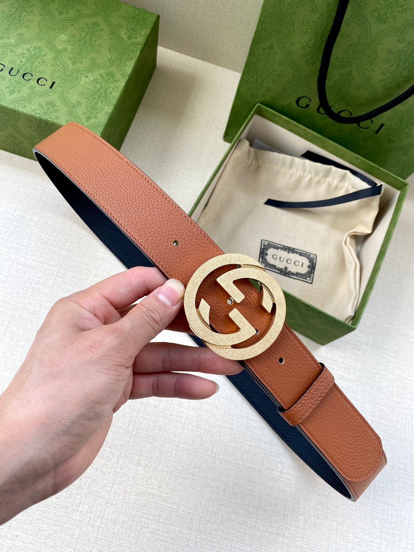 Gucci belt with tan leather strap and silver GG buckle, shown in hand