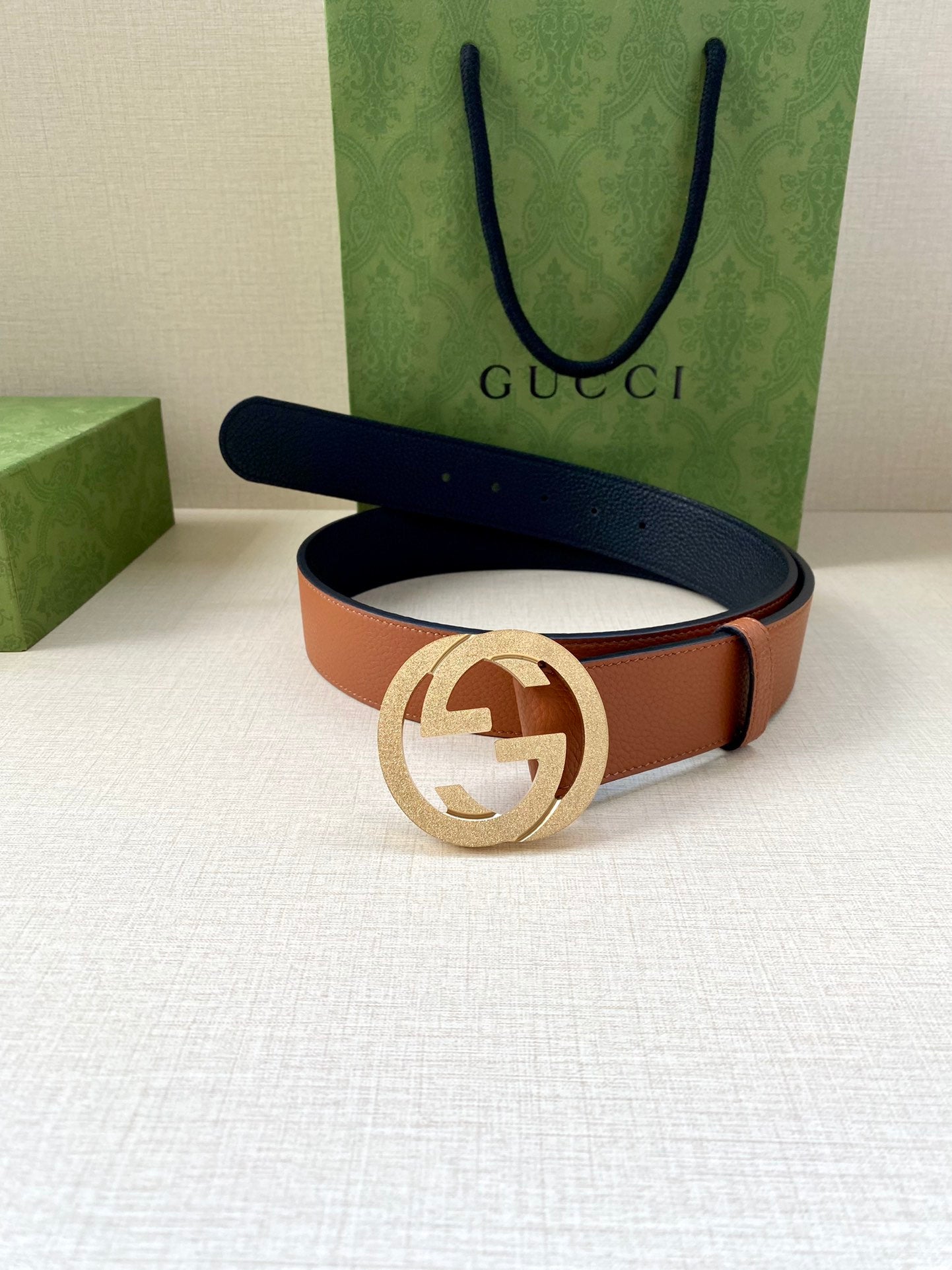 Gucci belt lying flat with tan leather and navy reverse, silver GG buckle