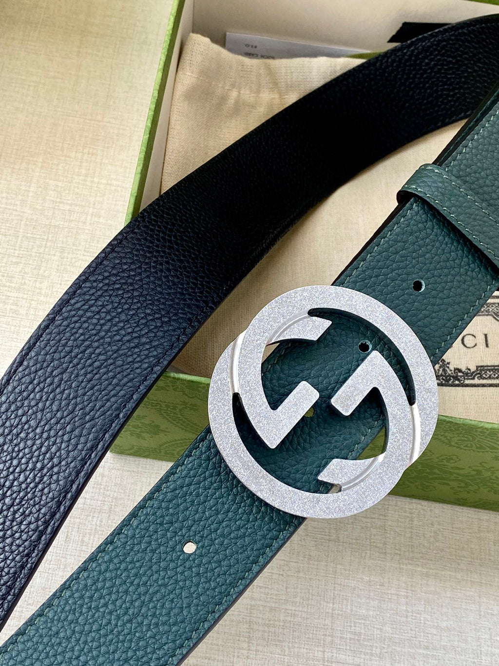 Teal leather belt with raised texture and silver interlocking logo buckle