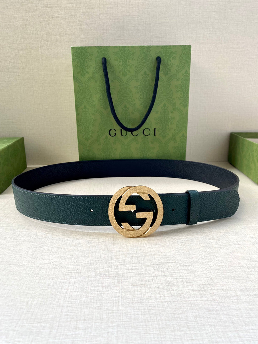 Teal leather belt with gold-tone interlocking logo buckle, laid flat