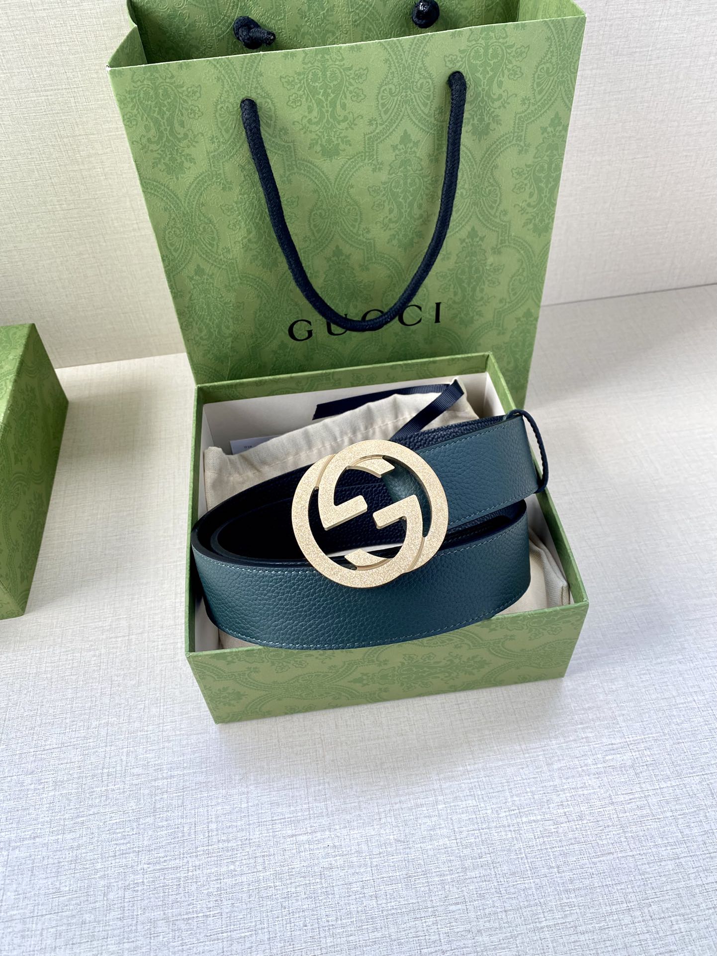Teal leather belt with interlocking logo buckle inside green gift box