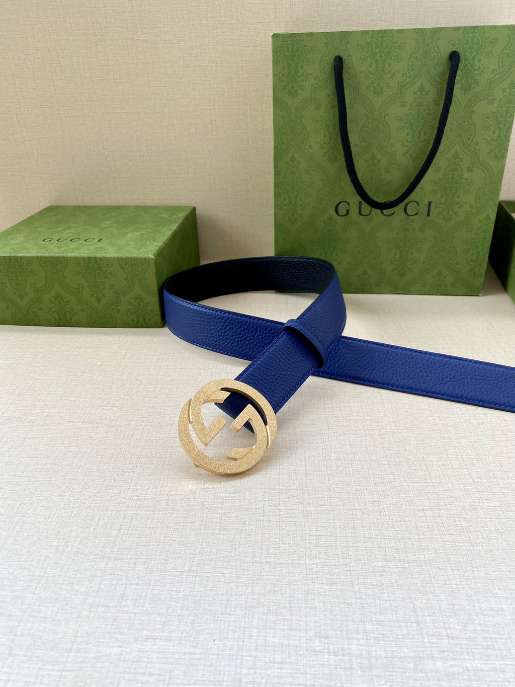 Gucci belt with blue strap and gold-toned GG buckle on a dark belt loop