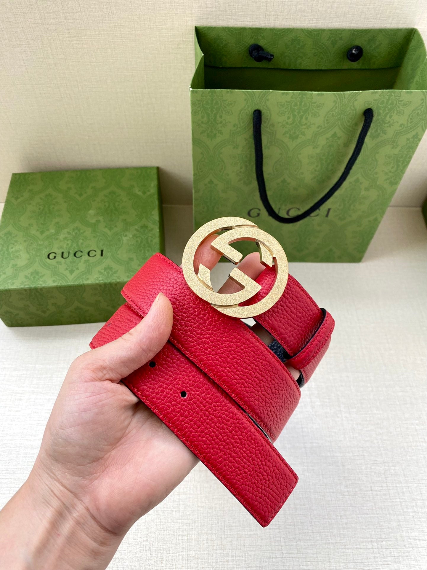 Red leather belt with gold-tone interlocking G buckle, held by hand, holes visible