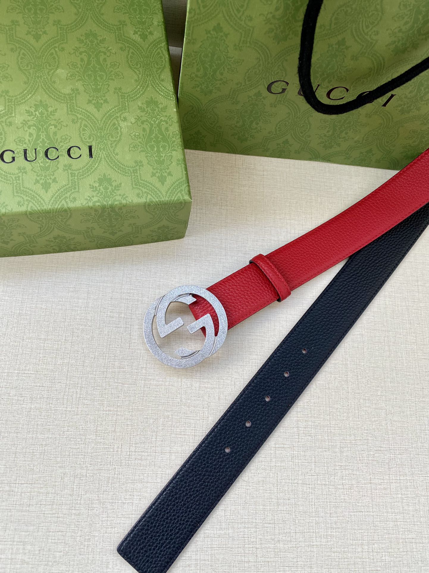 Red leather belt end with silver-tone interlocking G buckle, navy strap beside it