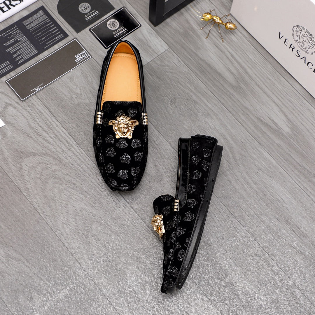 Black luxury loafers with gold Medusa emblem on patterned fabric and tan lining