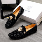 Pair of black patterned luxury loafers with gold Medusa emblem and tan interior
