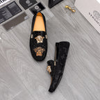 Black loafers pair, one upside view, gold-tone emblem on textured vamp