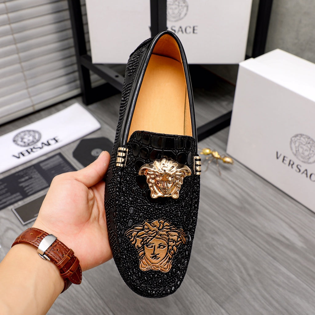 Black loafer held in hand, croc-look panel with gold Medusa and coin hardware