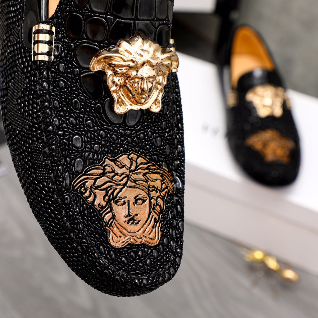 Black loafer close-up with gold Medusa emblem and embossed face graphic
