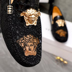 Black loafer close-up with gold Medusa emblem and embossed face graphic