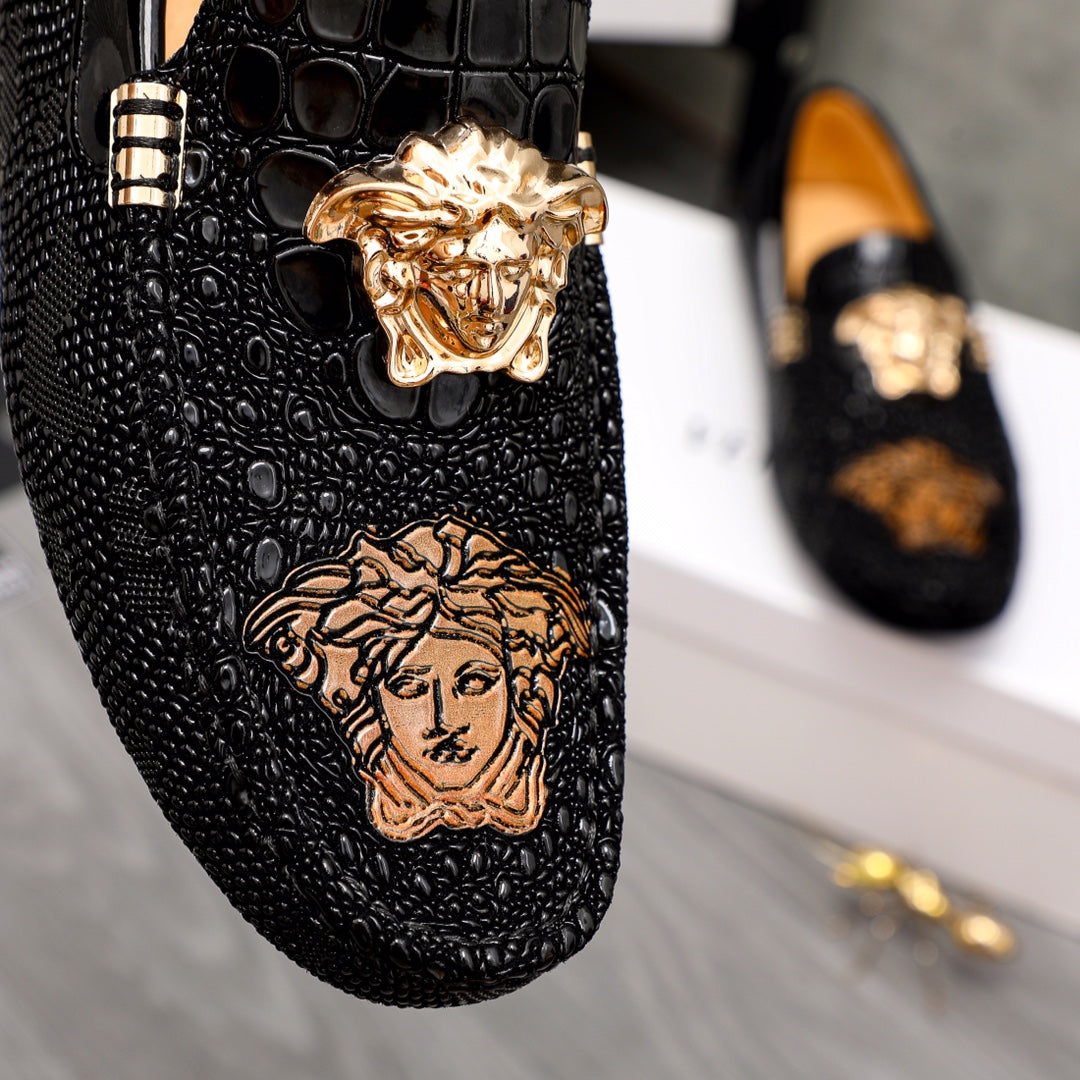 Black loafer close-up with gold Medusa emblem and embossed face graphic
