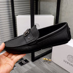 Versace black slip-on loafer held in hand, textured upper and logo buckle